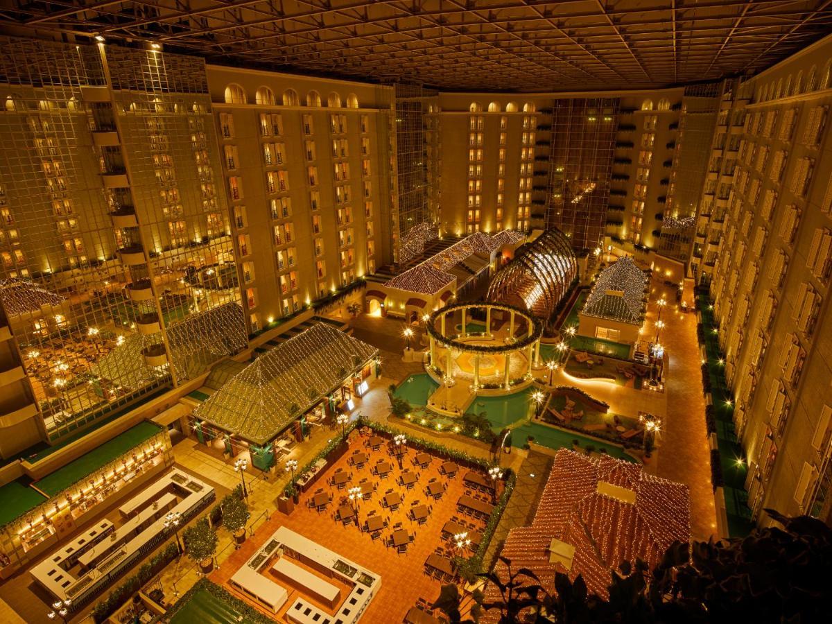 Grand Nikko Tokyo Bay Maihama Hotel Urayasu Exterior foto The photo shows a large, illuminated atrium of a hotel or resort complex. Several floors of what appear to be guest rooms or apartments surround the central area. The atrium contains a variety of amenities, including a pool or water feature, landscap