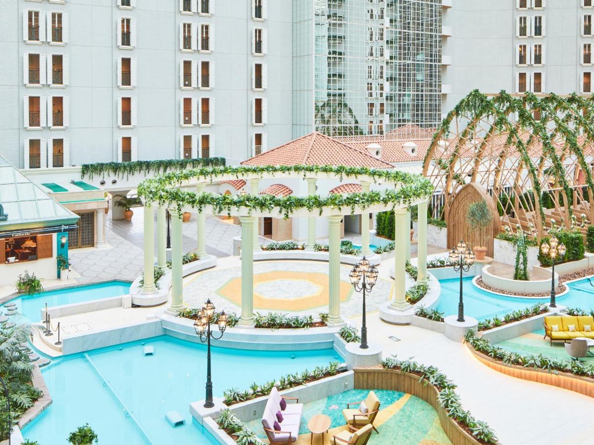 Grand Nikko Tokyo Bay Maihama Hotel Urayasu Exterior foto The photo shows a beautifully landscaped outdoor area, likely part of a resort or hotel. It features a central circular structure supported by white columns, decorated with greenery. Surrounding this structure are several swimming pools or water feat