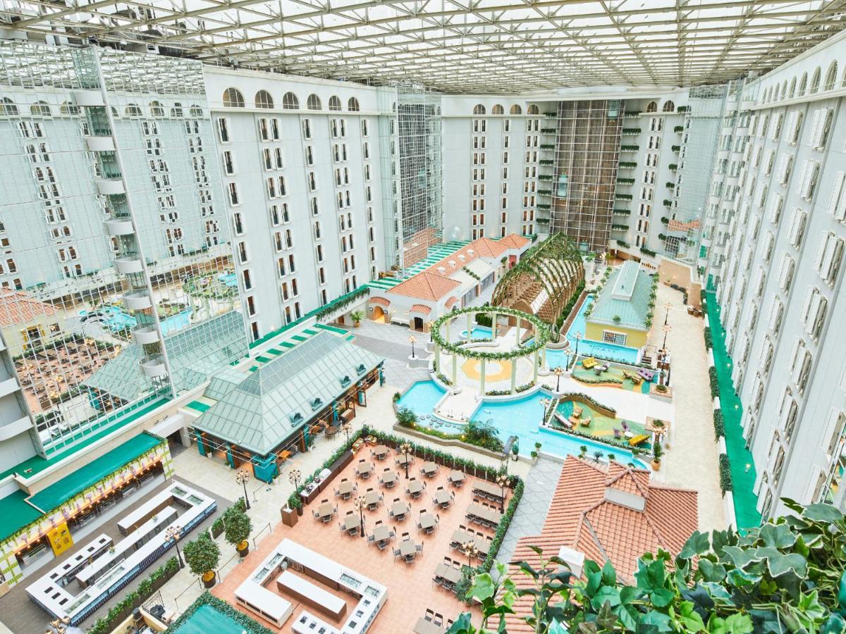 Grand Nikko Tokyo Bay Maihama Hotel Urayasu Exterior foto The photo depicts a large indoor area, likely within a resort or hotel, featuring a spacious atrium. The atrium has a glass roof, allowing natural light to flood the space. In the center, there are various swimming pools and a lush, green landscape w