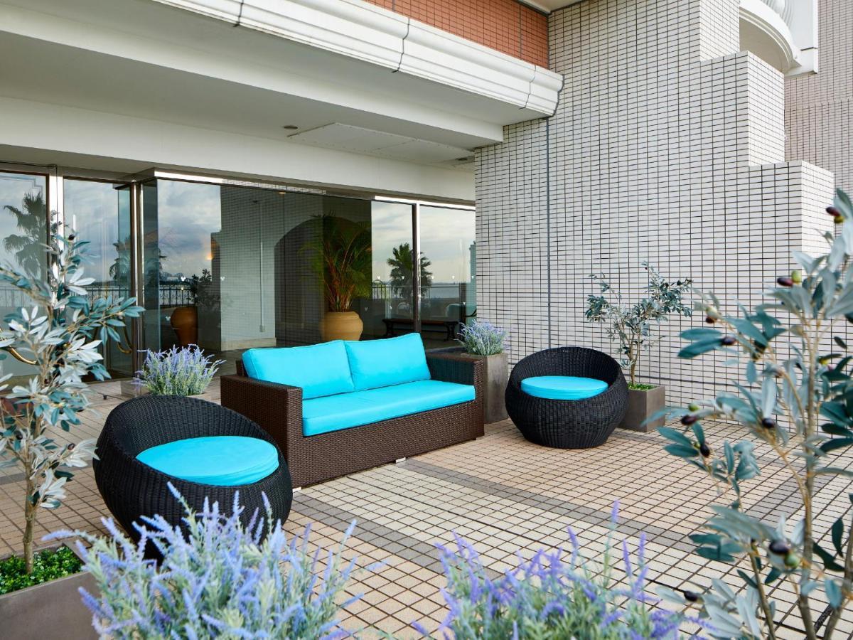 Grand Nikko Tokyo Bay Maihama Hotel Urayasu Exterior foto The image shows a stylish outdoor seating area. There is a brown couch with turquoise cushions, complemented by two matching round chairs nearby. The seating is arranged on a tiled patio, which is bordered by planters featuring lavender flowers and g
