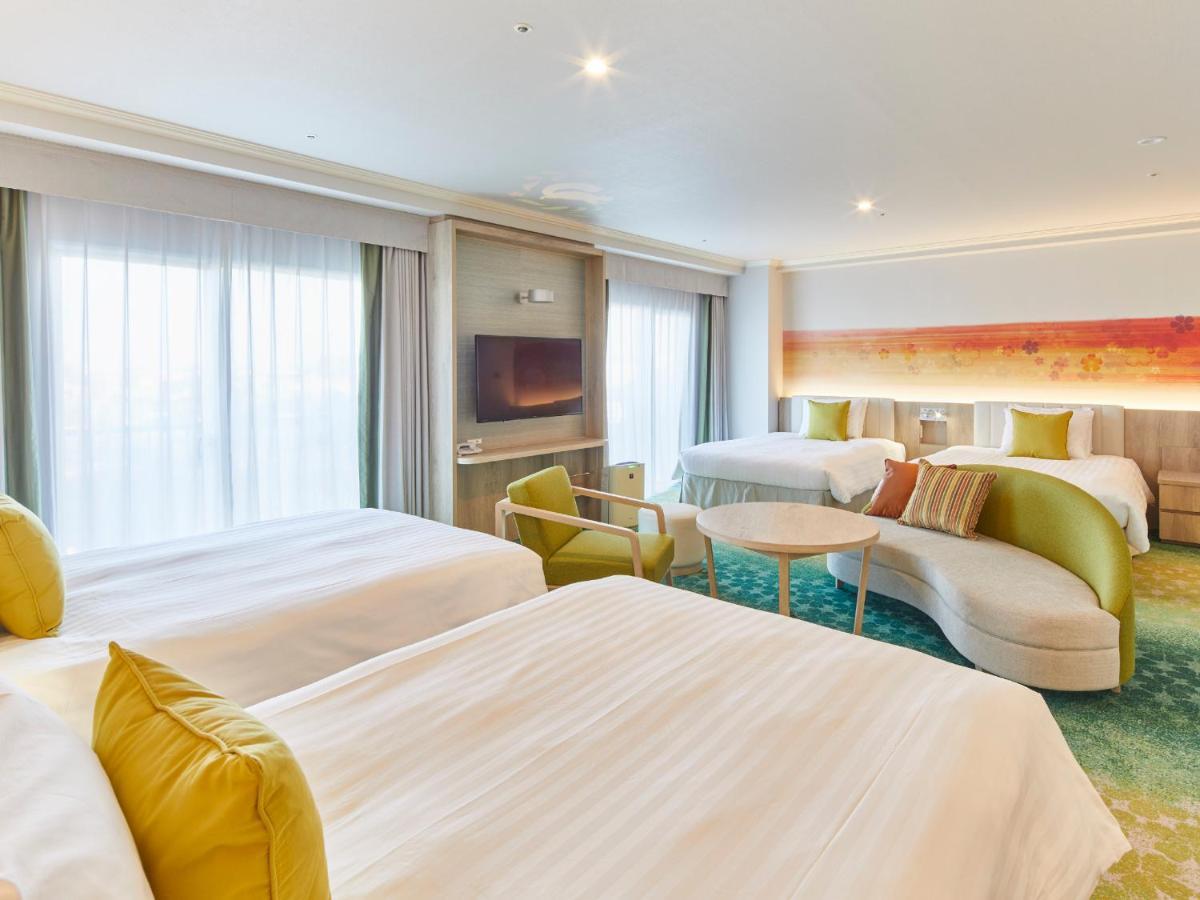 Grand Nikko Tokyo Bay Maihama Hotel Urayasu Exterior foto The photo shows a modern hotel room that features two large beds covered with white bedding and decorative pillows. There is a contemporary, curved sofa in a light color, along with a round table in the middle. The room has large windows that allow n