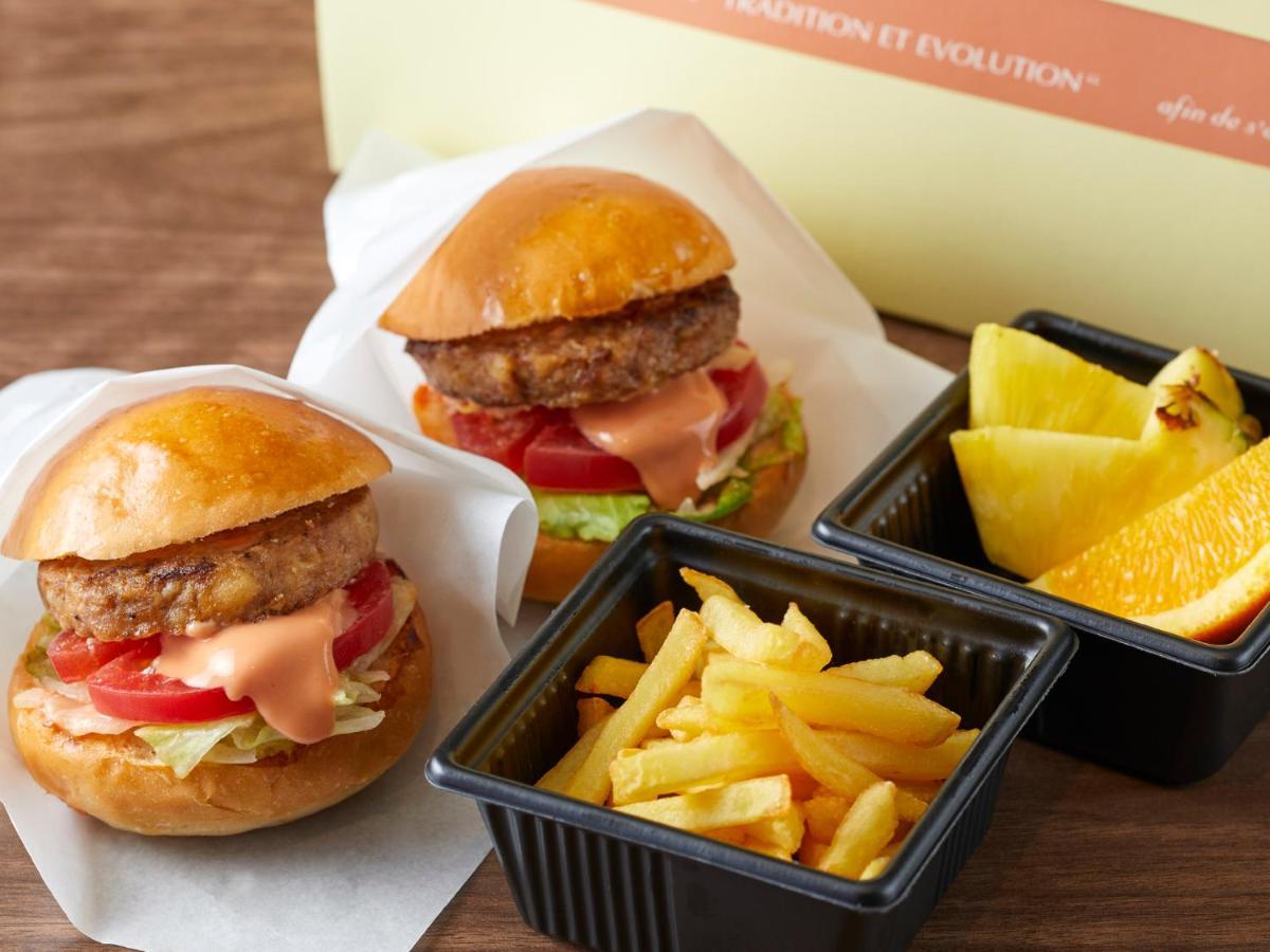 Grand Nikko Tokyo Bay Maihama Hotel Urayasu Exterior foto The photo shows two small burgers placed on a white background, each with a golden-brown bun, a fried patty, lettuce, tomato, and a creamy sauce. Alongside the burgers, there are two containers: one holding a serving of french fries and the other con