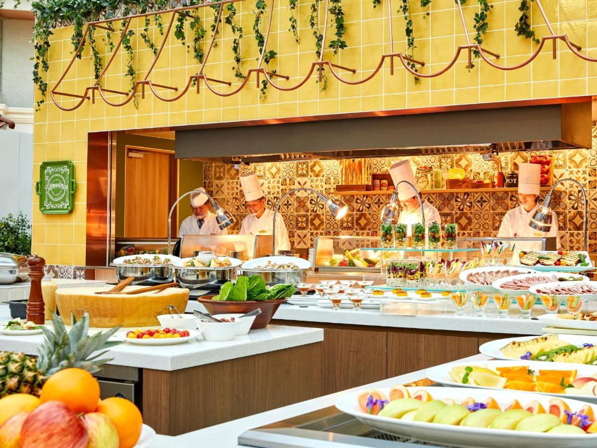 Grand Nikko Tokyo Bay Maihama Hotel Urayasu Exterior foto The photo shows a vibrant and colorful buffet setup in a restaurant. In the foreground, there are various dishes arranged on white platters, featuring an assortment of fruits, desserts, and other items. The background features chefs in white uniforms