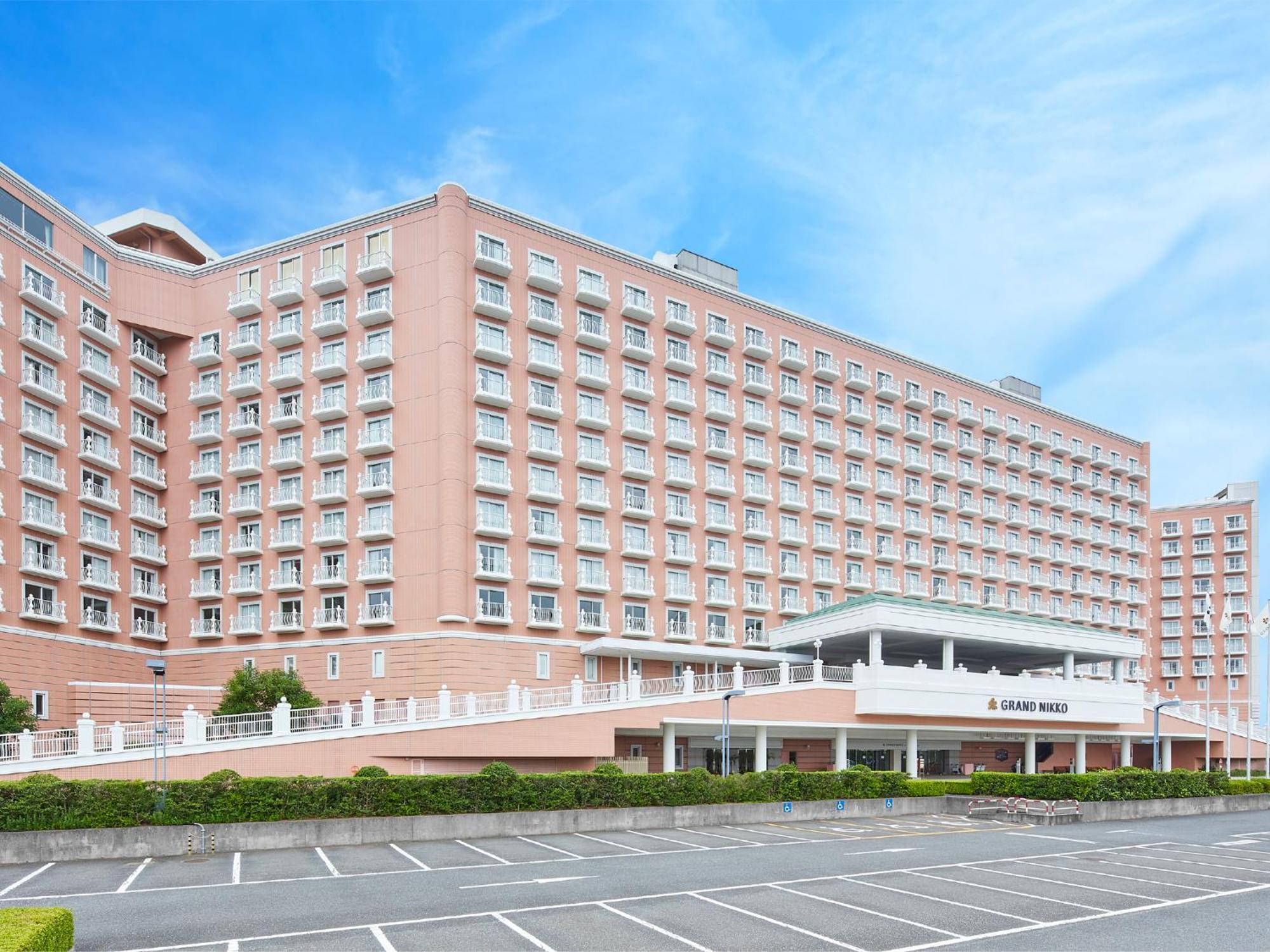 Grand Nikko Tokyo Bay Maihama Hotel Urayasu Exterior foto The photo shows a large, multi-story hotel building, characterized by its pink facade and modern architectural design. The structure features numerous windows and a spacious entrance area, complemented by a canopy. In front of the hotel, there is a p