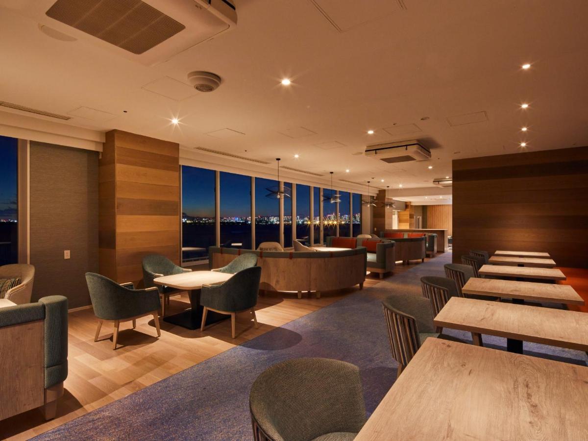 Grand Nikko Tokyo Bay Maihama Hotel Urayasu Exterior foto The photo shows a modern, well-lit lounge or café area. It features a mix of seating options, including cozy armchairs and tables with chairs. The space has large windows displaying a view, likely of a city or landscape at dusk, given the nighttime a