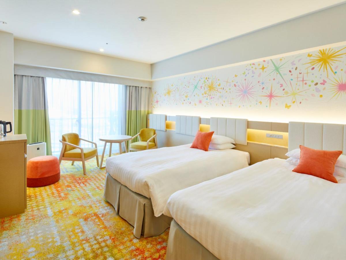 Grand Nikko Tokyo Bay Maihama Hotel Urayasu Exterior foto The photo shows a modern hotel room featuring two twin beds with light-colored bedding and decorative orange cushions. There is a vibrant, colorful carpet on the floor, and the walls are adorned with playful designs, including bursts of color. A larg