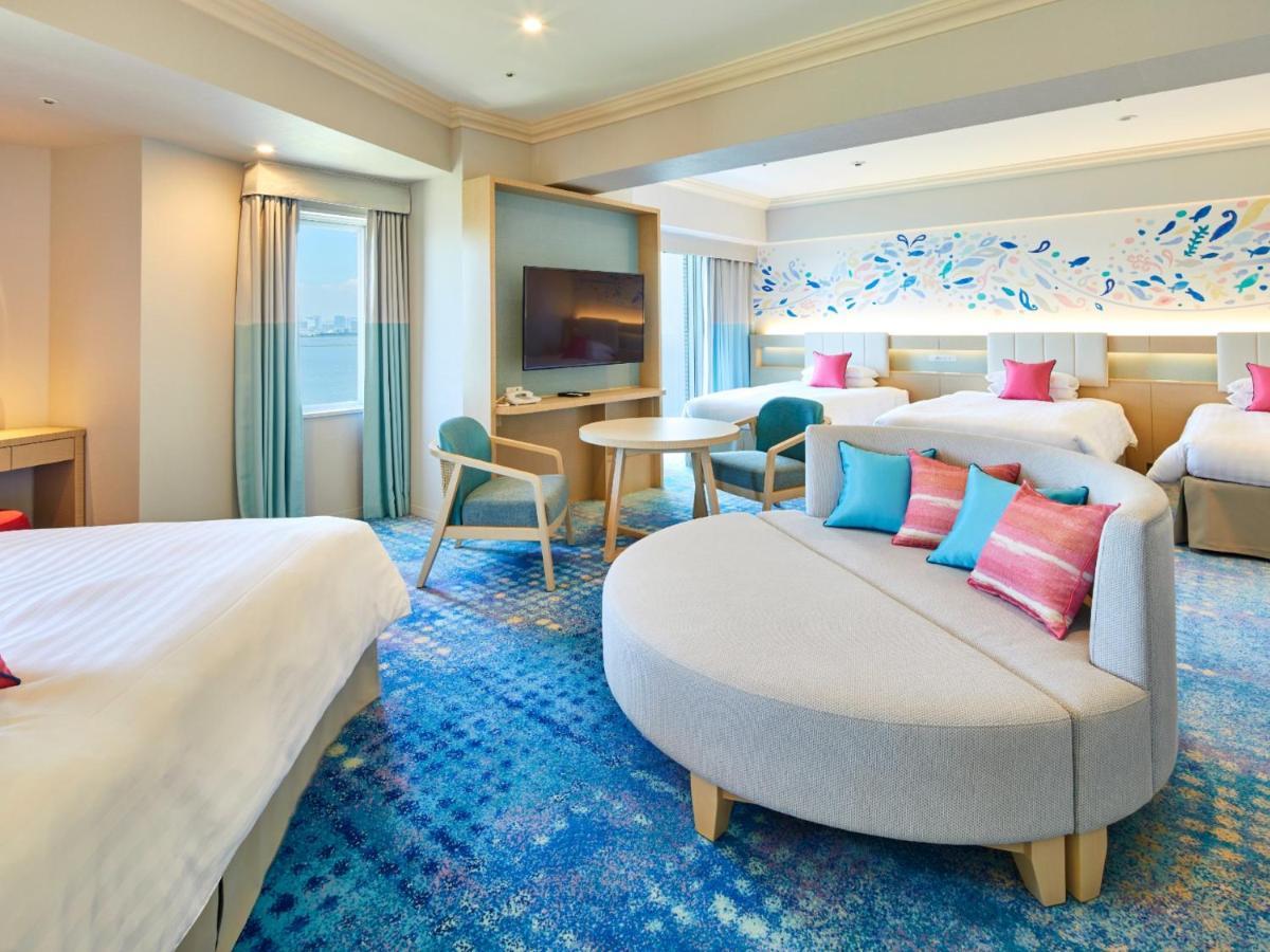 Grand Nikko Tokyo Bay Maihama Hotel Urayasu Exterior foto The photo shows a modern hotel room featuring a spacious layout with multiple beds. There is a large, curved sofa with colorful cushions in the center, adding a contemporary touch to the design. The room has large windows allowing natural light to fi