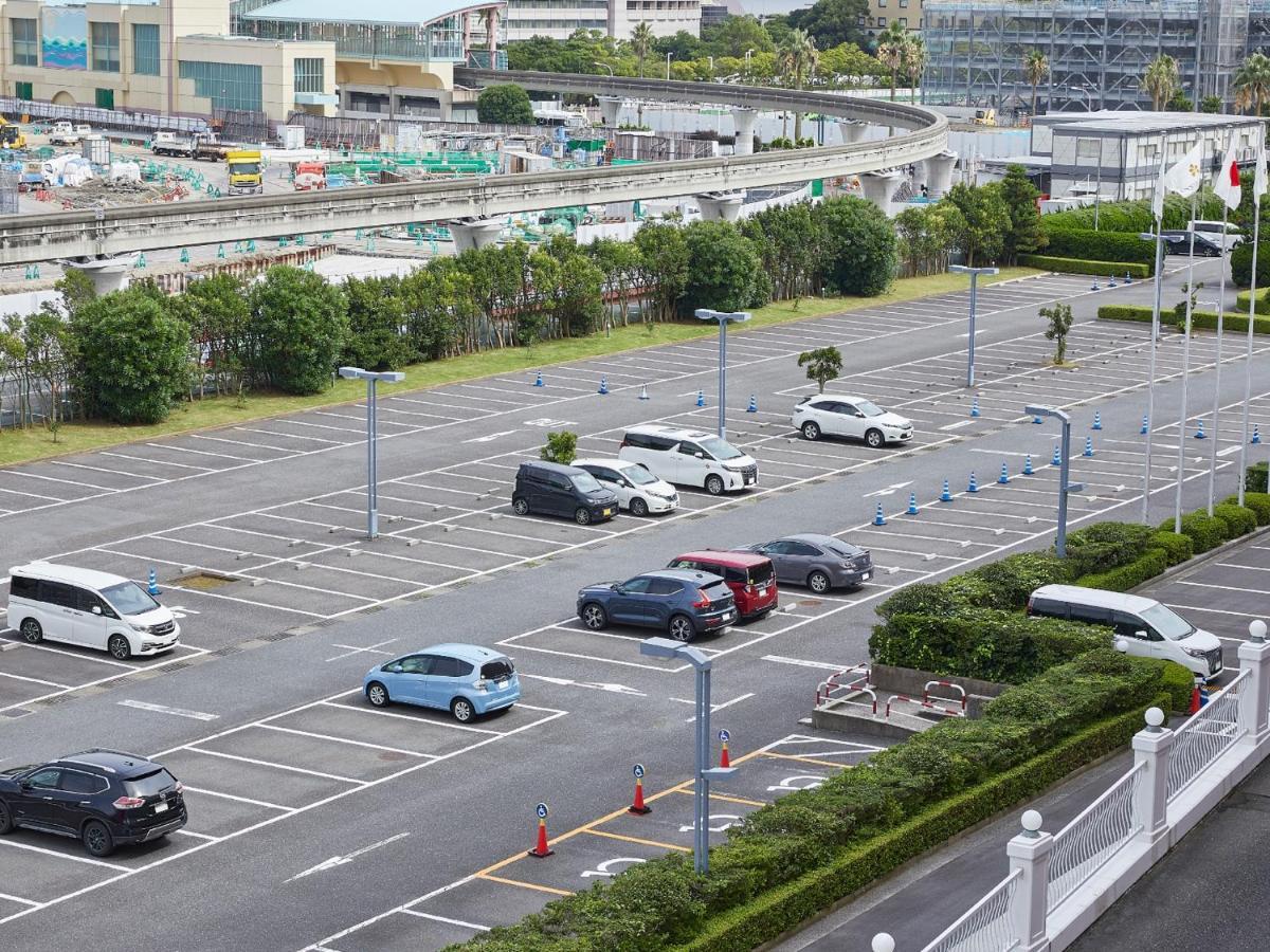 Grand Nikko Tokyo Bay Maihama Hotel Urayasu Exterior foto The photo shows a partially empty parking lot with several parked cars. In the foreground, there are a few vehicles, including a blue car and a white one. The lot has clearly marked parking spaces, and there are some trees and shrubs along the sides.