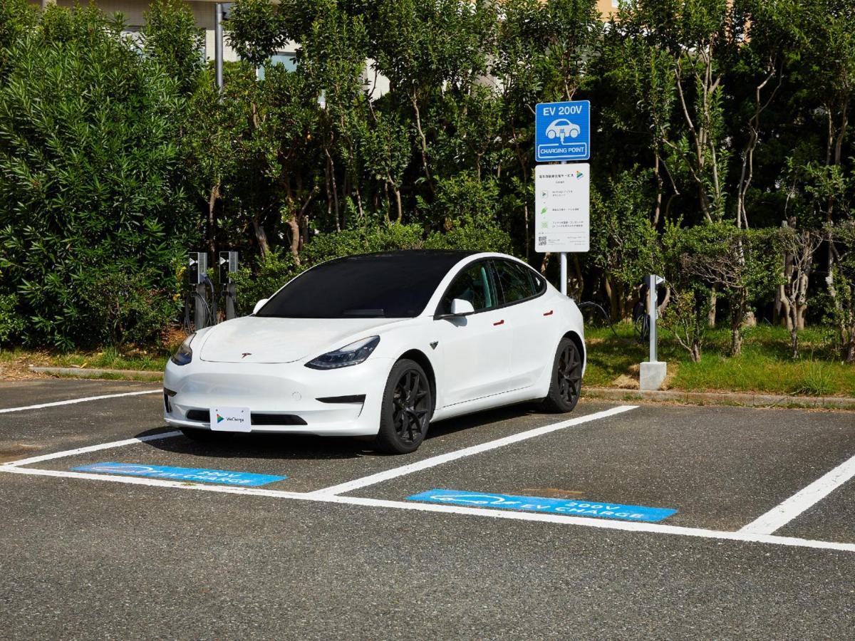 Grand Nikko Tokyo Bay Maihama Hotel Urayasu Exterior foto The photo shows a white electric car parked in an EV (electric vehicle) charging spot. The car has a sleek design with black wheels and tinted windows. In the background, there are green shrubs and trees, indicating a natural or landscaped environmen