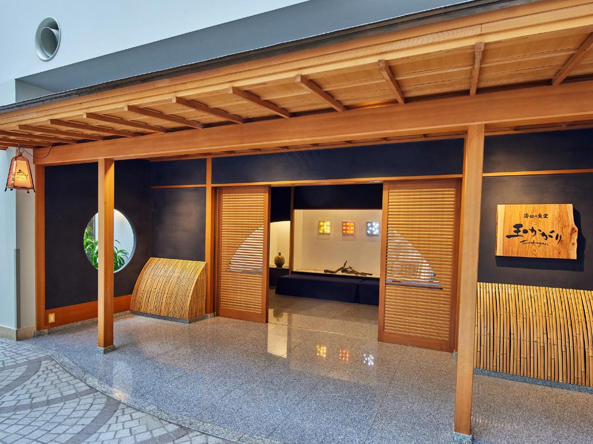 Grand Nikko Tokyo Bay Maihama Hotel Urayasu Exterior foto The photo shows the entrance of a building, designed in a traditional Japanese style. It features a wooden structure with a large overhanging roof and sliding doors. The entrance is flanked by rounded windows, and there's a decorative sign with Japan
