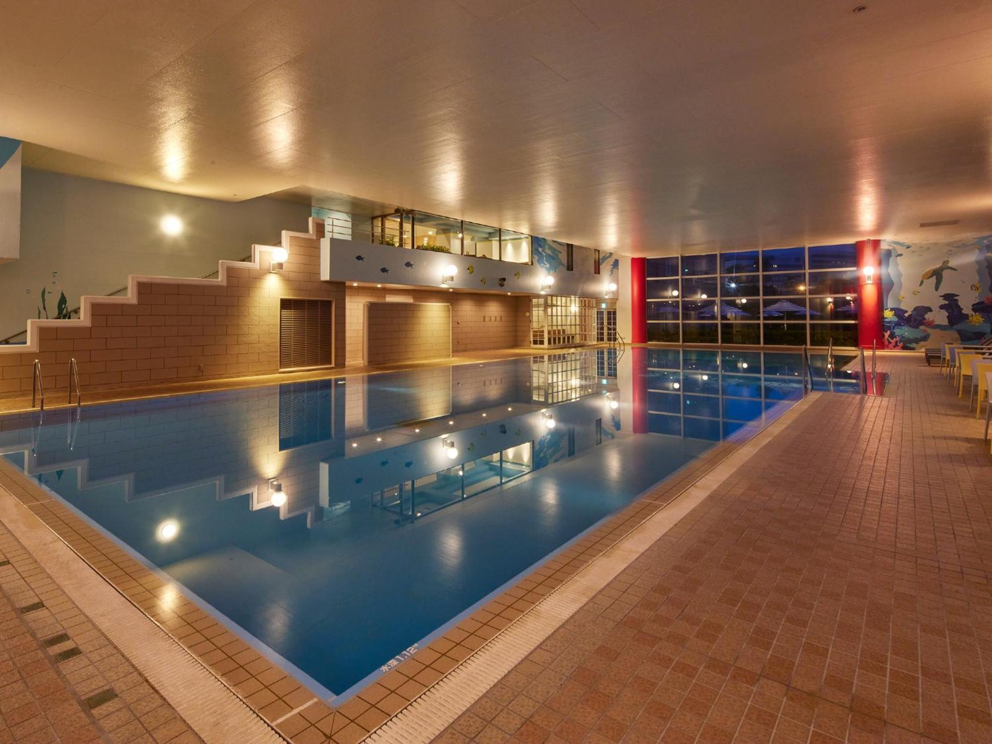 Grand Nikko Tokyo Bay Maihama Hotel Urayasu Exterior foto The photo shows an indoor swimming pool area. The pool features a calm blue water surface and is surrounded by tiled flooring. There is a staircase leading to a higher level, likely providing access to a lounge or seating area. Large windows allow na