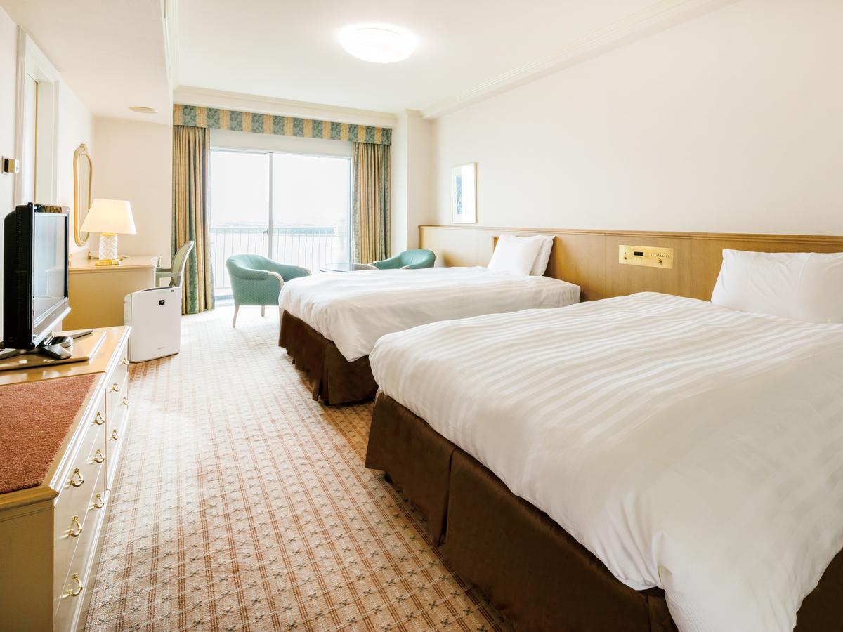 Grand Nikko Tokyo Bay Maihama Hotel Urayasu Exterior foto The photo shows a hotel room featuring two large beds with white bedding and brown bases. There's a light-colored carpet on the floor, and the room is brightly lit. To one side, there is a television on a stand and a small white refrigerator. A desk 
